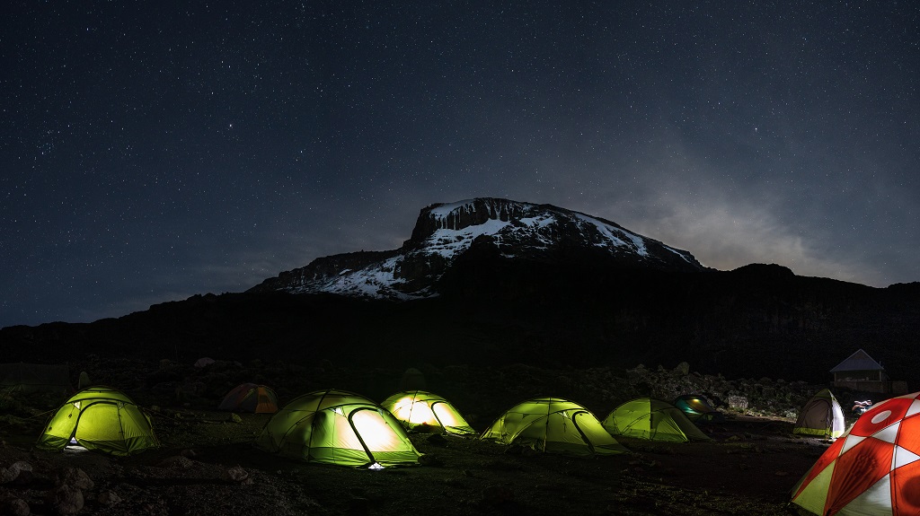 Lighted tents in the night in front of Mount Kilimanjaro